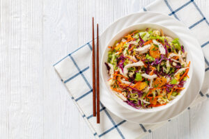 Egg Roll in a bowl with shredded chicken meat, mandarin oranges, crunchy noodles, red cabbage, napa cabbage, carrots, green onions in bowl, flat lay, free space